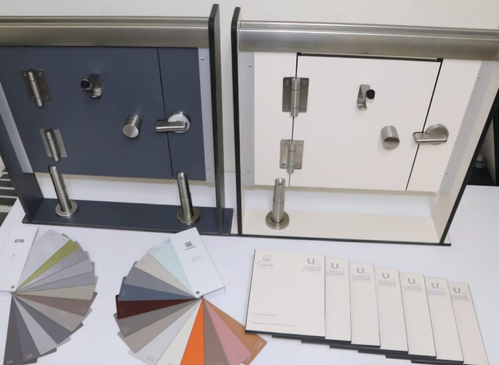 نموذج تركيب قواطيع حمامات متكامل يشمل الأبواب والمفصلات والأقفال مع عينات ألوان متعددة، يوضح طريقة التنفيذ العملي لقواطيع حمامات كومباكت HPL في المشاريع التجارية مع التركيز على الجودة والمتانة في الاستخدام اليومي