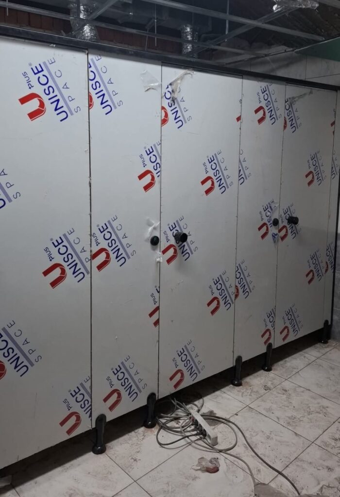 قواطيع حمامات HPL أثناء مرحلة التركيب داخل موقع العمل، باستخدام ألواح كومباكت مقاومة للمياه مع قواعد تثبيت قوية، تنفيذ عملي مناسب لدورات المياه في المصانع والمباني التجارية بالقاهرة