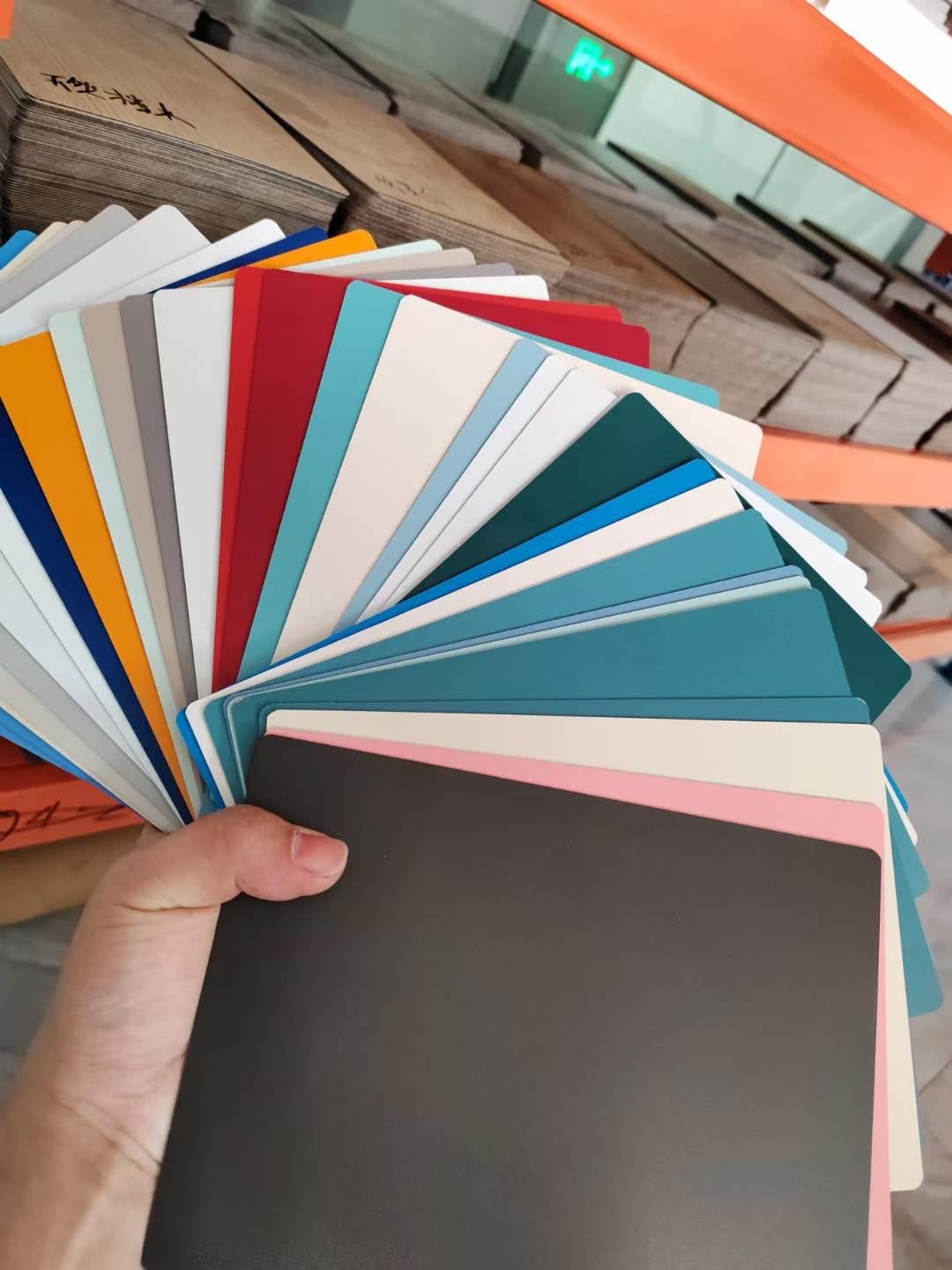 Wide compact HPL colour fan held in front of warehouse stock at Cairo House in New Nozha, Cairo, from bright shades to soft neutrals. Clients use this range to spec Compact HPL in Cairo panels for interior and joinery projects.