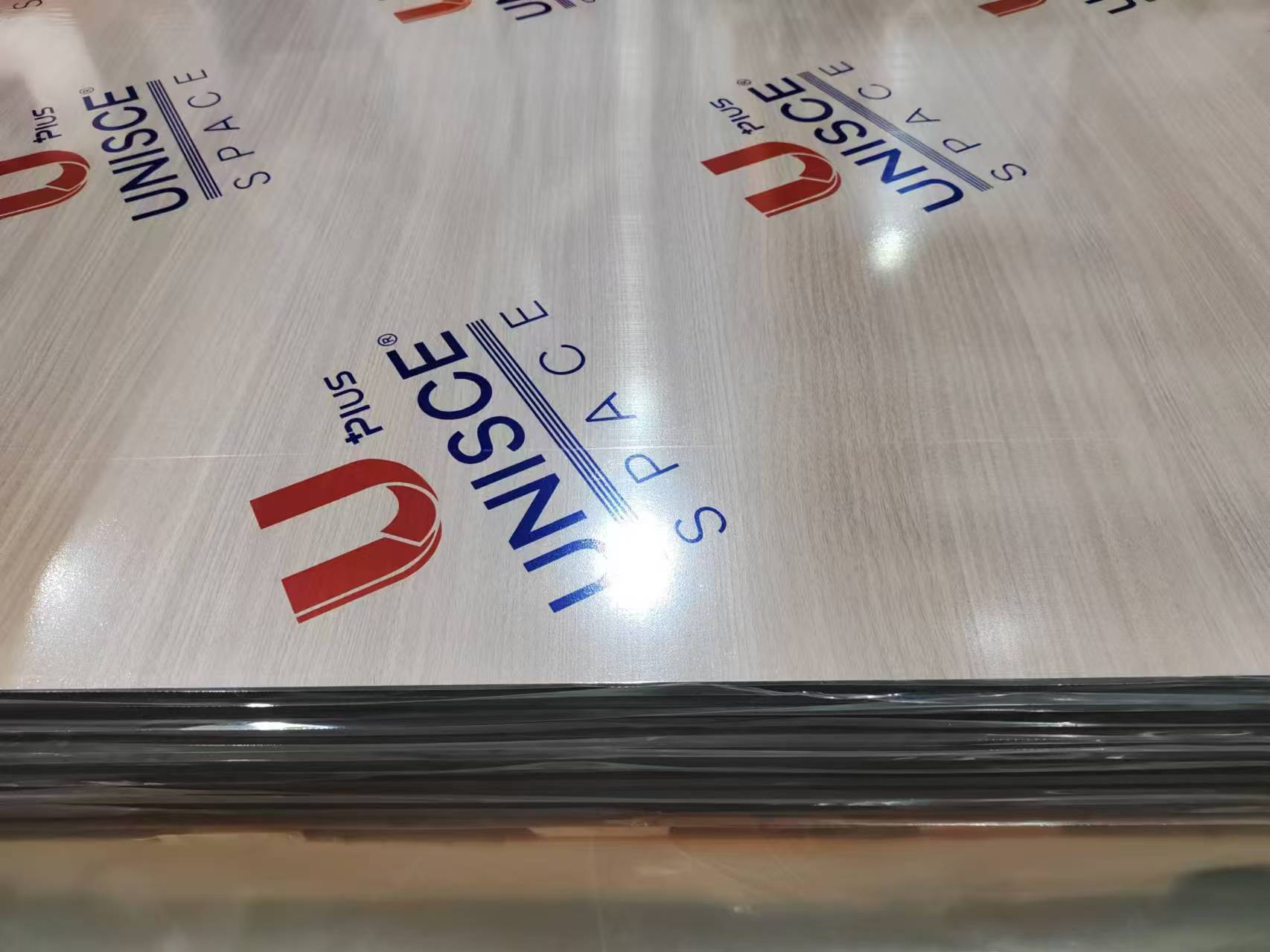 Close view of a light wood grain compact HPL sheet surface, still under factory film. The grain print and scratch resistant top layer are what make Compact HPL in Cairo a durable choice for wall cladding, toilet cubicles and worktops.