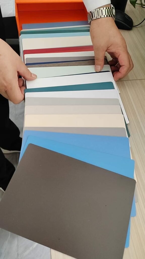 Hands opening a compact HPL swatch book of solid colours from teal and blue to cream and grey at Cairo House in New Nozha, Cairo. The bound samples help clients shortlist Compact HPL in Cairo panel colours for interior fit out.