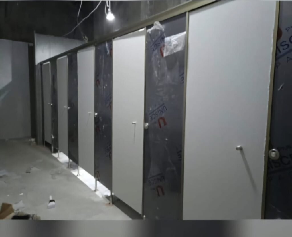 Compact HPL toilet cubicle partitions being installed on site, still under protective film, supplied and fitted by Cairo House in New Nozha, Cairo. Moisture resistant Compact HPL in Cairo makes durable washroom cubicles that last.