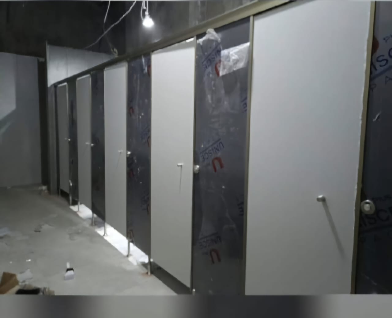 Compact HPL toilet cubicle partitions being installed on site, still under protective film, supplied and fitted by Cairo House in New Nozha, Cairo. Moisture resistant Compact HPL in Cairo makes durable washroom cubicles that last.