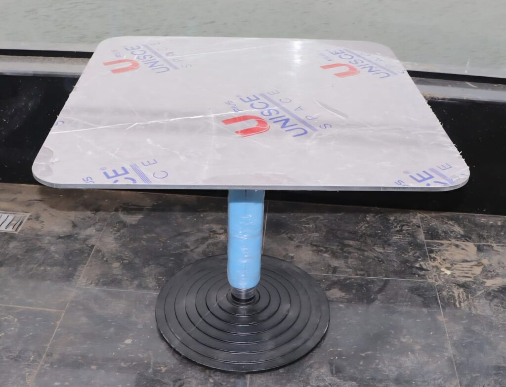 Square grey Corian cafe countertop on a black pedestal base supplied by Cairo House, still wrapped at a Cairo waterfront venue, part of the custom Corian Tables in Cairo installed for cafes and restaurants across the city.
