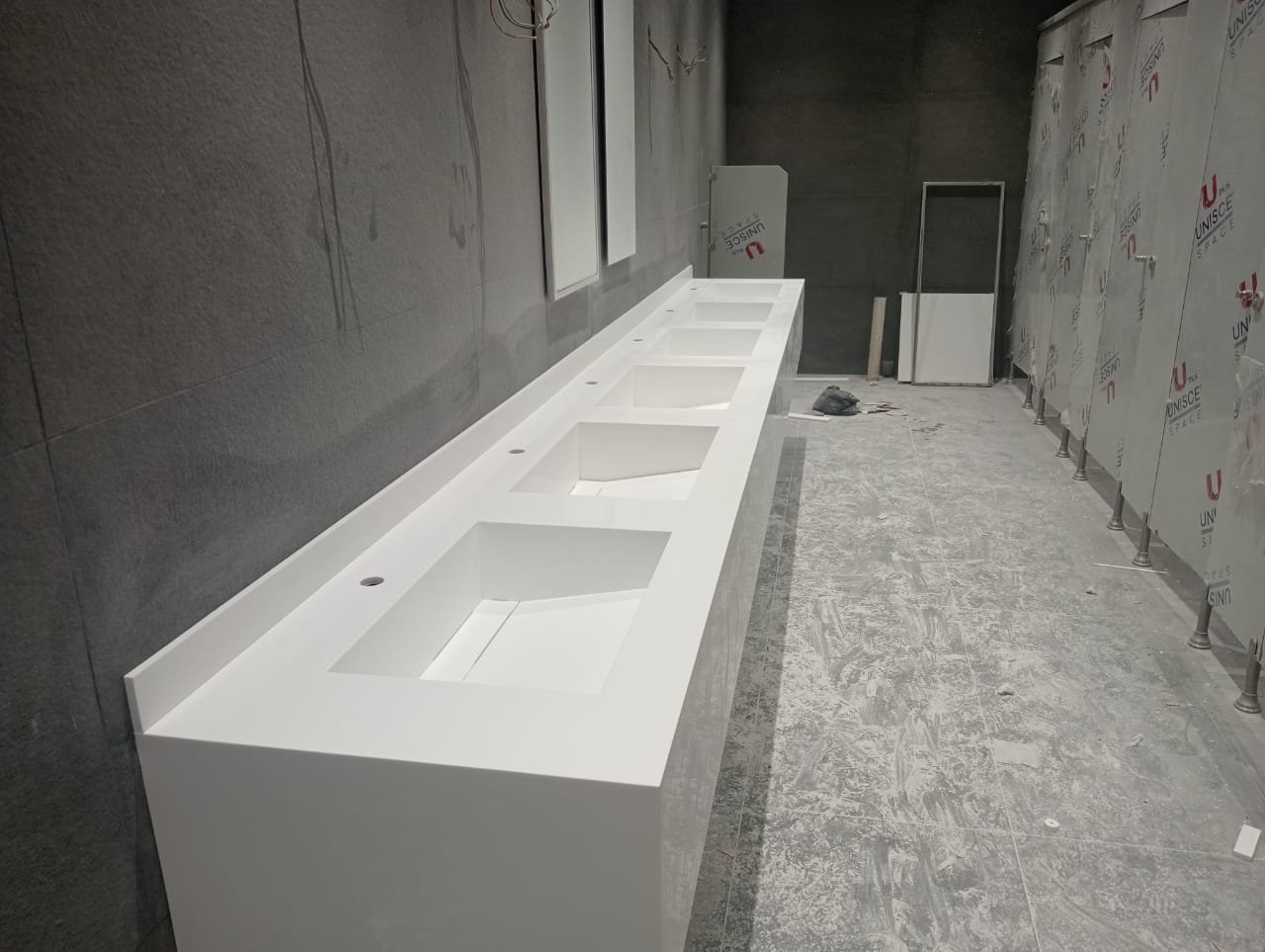 Seamless white Corian solid surface vanity trough with integrated moulded basins installed by Cairo House in a commercial washroom in Cairo, compact HPL partitions behind, showing one continuous surface with no join between the counter and the sinks.