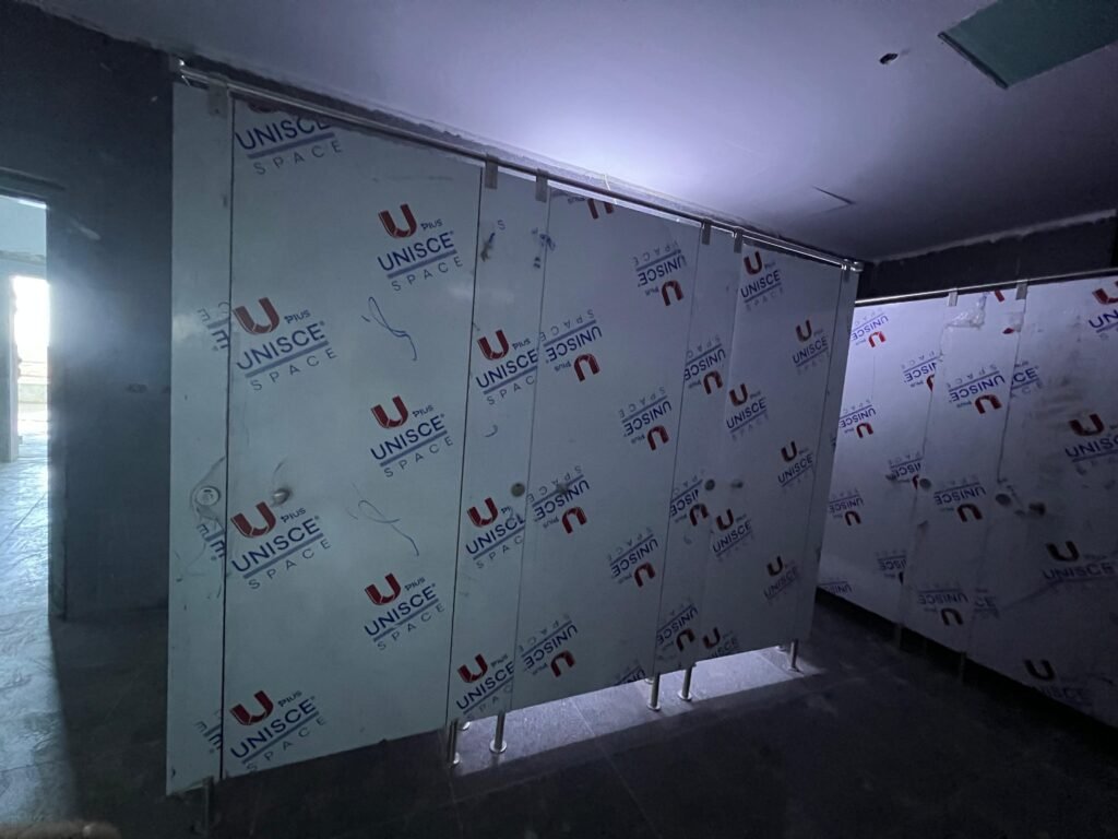 Compact HPL partitions in Cairo standing under blue UNISCE film in a stripped washroom. Cairo House is the exclusive UNISCE agent in Egypt for compact HPL bathroom partitions and supplies direct into Cairo.