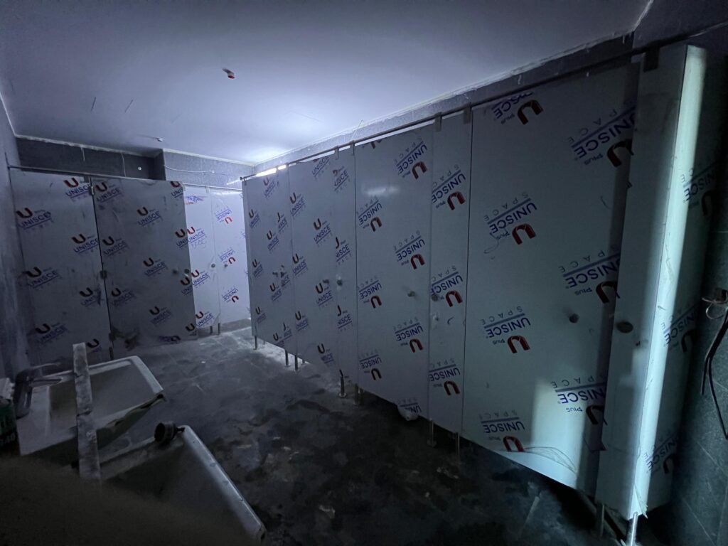 Compact HPL partitions in Cairo part way through installation, panels still carrying blue UNISCE film. Cairo House installs compact HPL bathroom partitions with its own crews on commercial projects around Cairo.