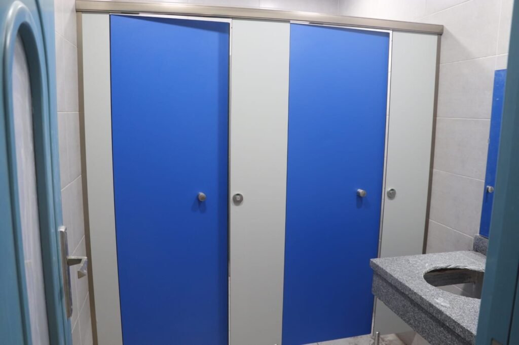 Blue and white compact HPL partitions in Cairo mid installation. Two tone layouts are a simple way to mark accessible cubicles without signage, and the colour is pressed through the compact HPL bathroom partition panel.