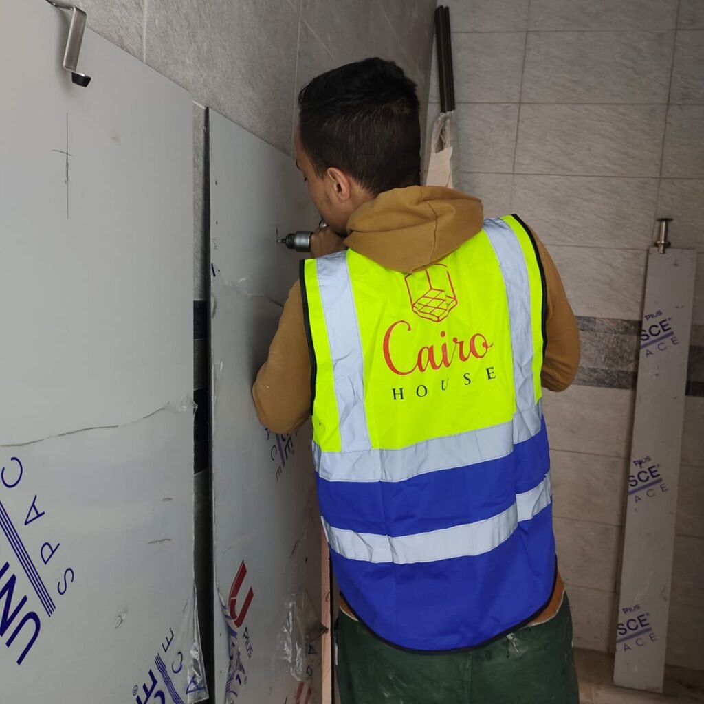 A Cairo House technician working on compact HPL partitions in Cairo. كايرو هاوس keeps installation in house, which is how compact HPL bathroom partition work in Cairo stays on programme and to specification.