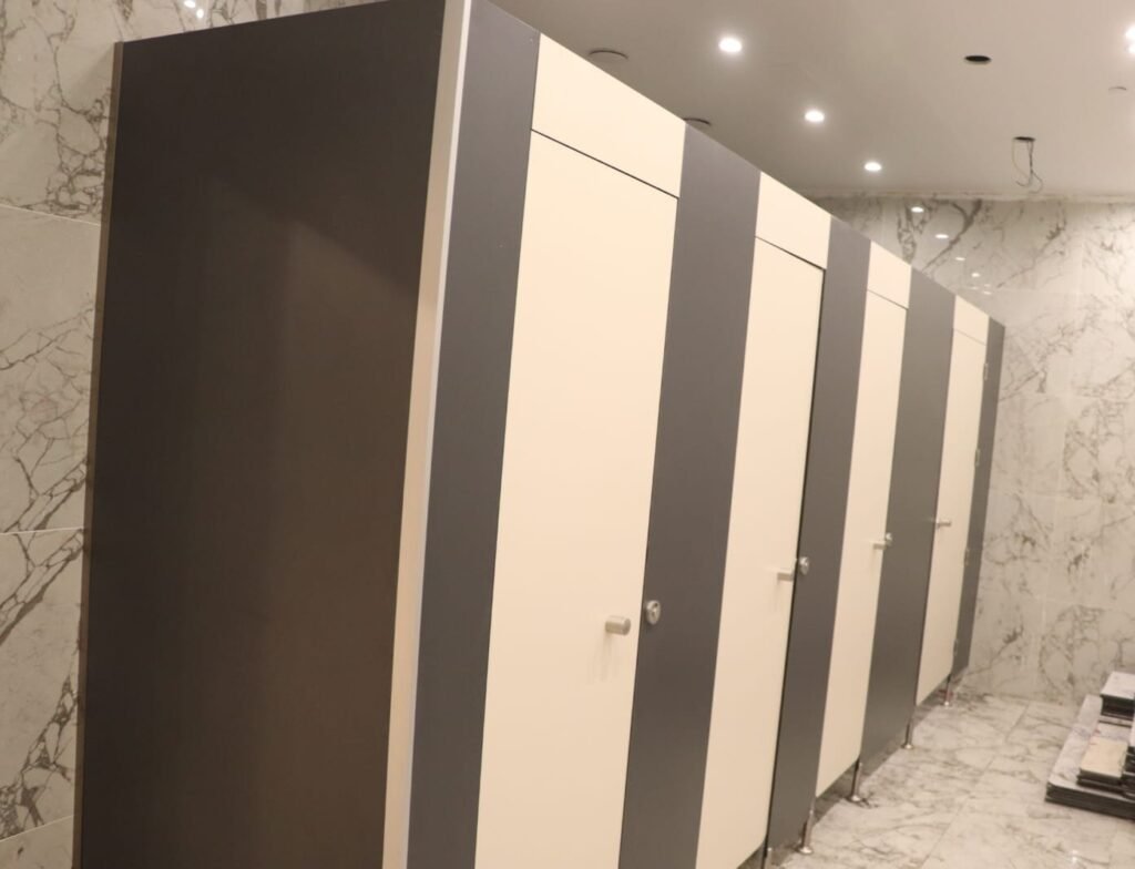 Charcoal and cream compact HPL partitions in Cairo set against a marble wall. Two tone compact HPL bathroom partition layouts are an easy way to break up a long washroom run on Cairo commercial projects.