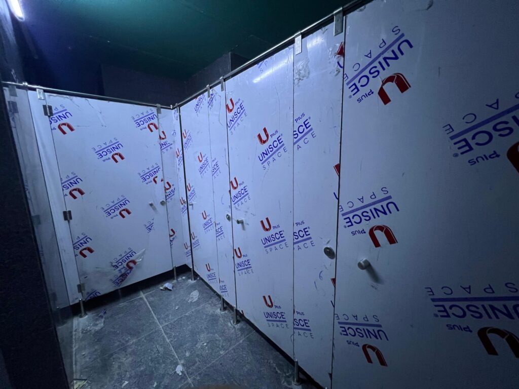 Corner run of compact HPL partitions in Cairo with the UNISCE film still on and locks fitted. Cairo House sets out compact HPL bathroom partitions from a site survey so the corner closes square on Cairo projects.