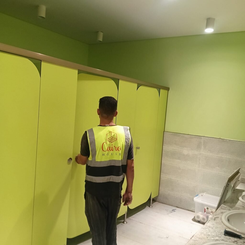 A Cairo House fitter hanging a lime green door on compact HPL partitions in Cairo. Doors on UNISCE compact HPL bathroom partitions are hung on stainless self closing hinges set to the angle the client asks for.