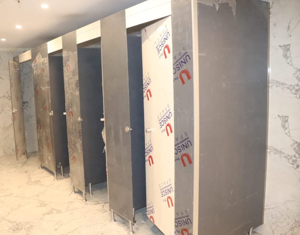 Grey compact HPL partitions in Cairo inside a marble lined washroom during handover checks. Cairo House supplies UNISCE compact HPL bathroom partitions with matching stainless hardware throughout Cairo.