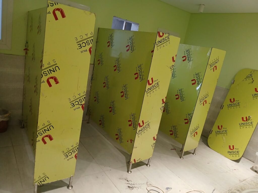 Lime green UNISCE boards for compact HPL partitions in Cairo standing ready for assembly. The film carries the UNISCE mark, the proof of origin behind every compact HPL bathroom partition Cairo House installs in Cairo.