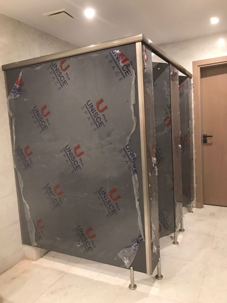 A UNISCE panel for compact HPL partitions in Cairo standing beside a timber door frame on site. Cairo House coordinates compact HPL bathroom partition colours with the joinery package on Cairo fit outs.