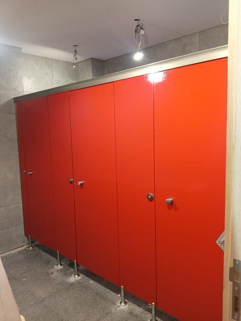 Bright red compact HPL partitions in Cairo with stainless steel knobs and indicator locks. The colour runs through the UNISCE panel, so compact HPL bathroom partitions in Cairo do not chip back to a pale core at the edges.