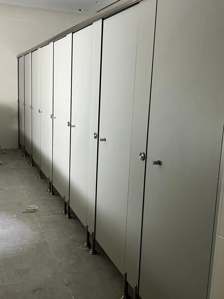 Sage grey compact HPL partitions in Cairo standing over an unfinished floor. Cairo House sets UNISCE compact HPL bathroom partitions on adjustable feet so final floor levels can still move without moving the cubicles.