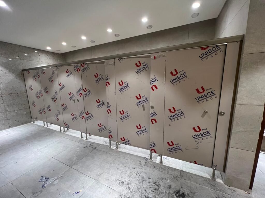 A finished run of sand toned compact HPL partitions in Cairo under downlights. Cairo House installs UNISCE compact HPL bathroom partitions with a floor gap that suits Egyptian cleaning practice in commercial washrooms.