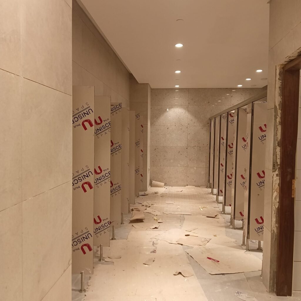 Sand tone compact HPL partitions in Cairo lining a lit washroom corridor finished in marble. Cairo House matches UNISCE compact HPL bathroom partition colours to the architect specification on commercial fit outs in Cairo.