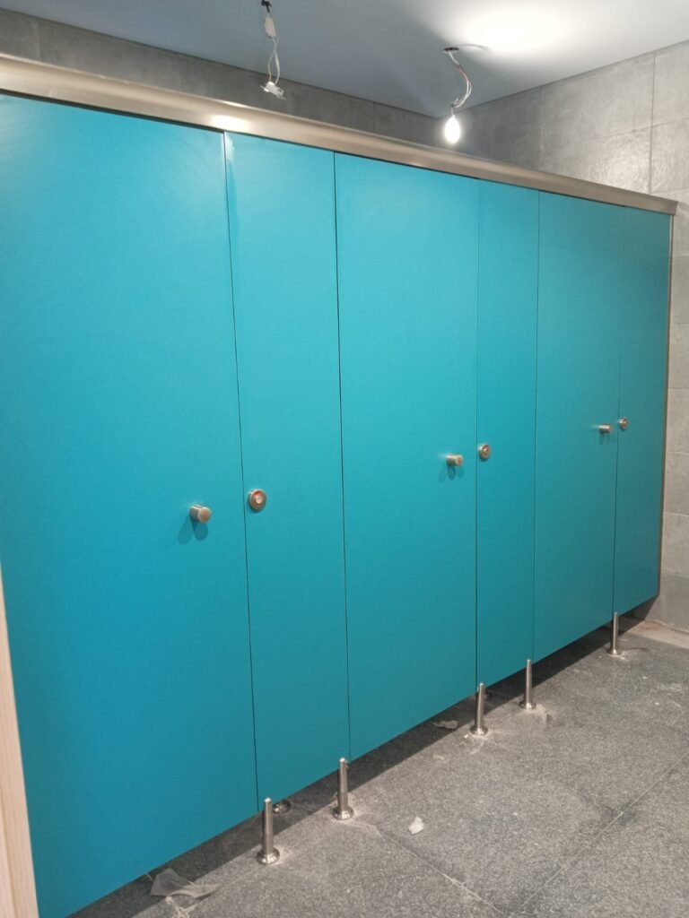 Turquoise compact HPL partitions in Cairo fitted with stainless hardware. Cairo House carries the full UNISCE colour range, letting clients pick compact HPL bathroom partitions that match the brand palette of the building.