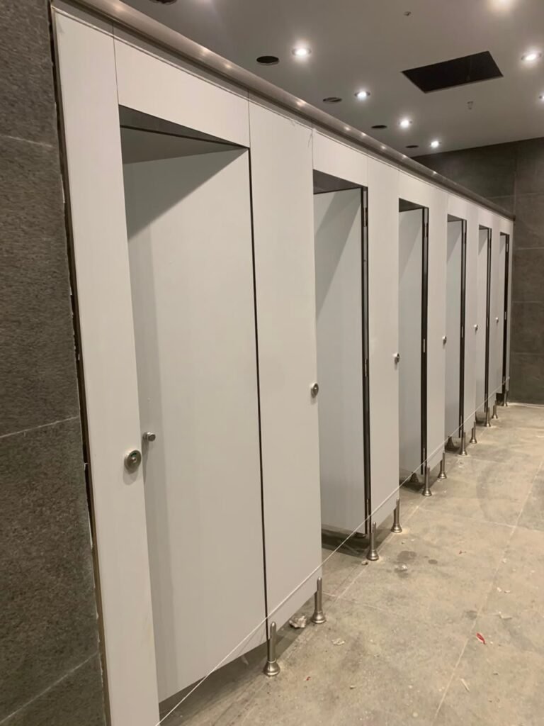 White and grey compact HPL partitions in Cairo standing over a marble floor. Cairo House sets UNISCE compact HPL bathroom partitions on adjustable stainless pilaster shoes so the panels stay clear of standing water.