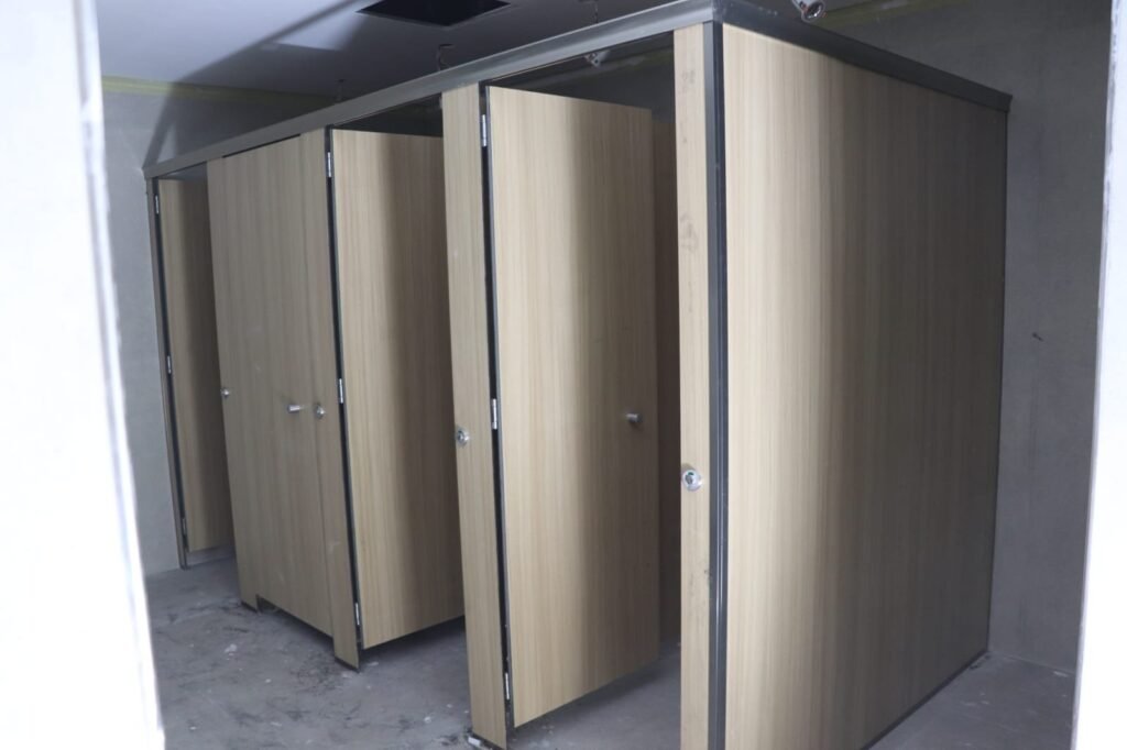 Wood grain compact HPL partitions in Cairo finished and handed over. The decorative layer is pressed into the UNISCE panel, so compact HPL bathroom partitions in Cairo keep the timber look without any veneer to lift.