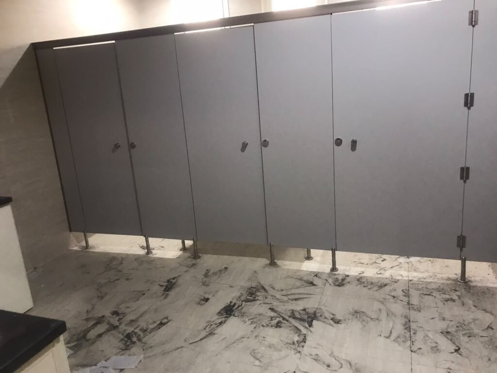 A run of mid grey compact HPL cubicles with steel legs and slim knob locks over a marble floor still dusty from works. Compact HPL in Cairo supplied and installed by Cairo House (كايرو هاوس - قواطيع حمامات كوريان و كومباكت HPL و ارضيات مرتفعة).